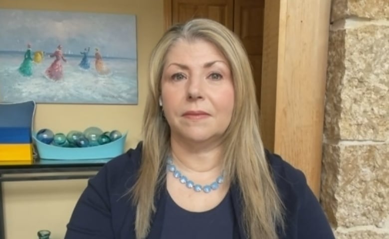 A woman with long blonde hair in a blue sweater faces the camera on a video call.