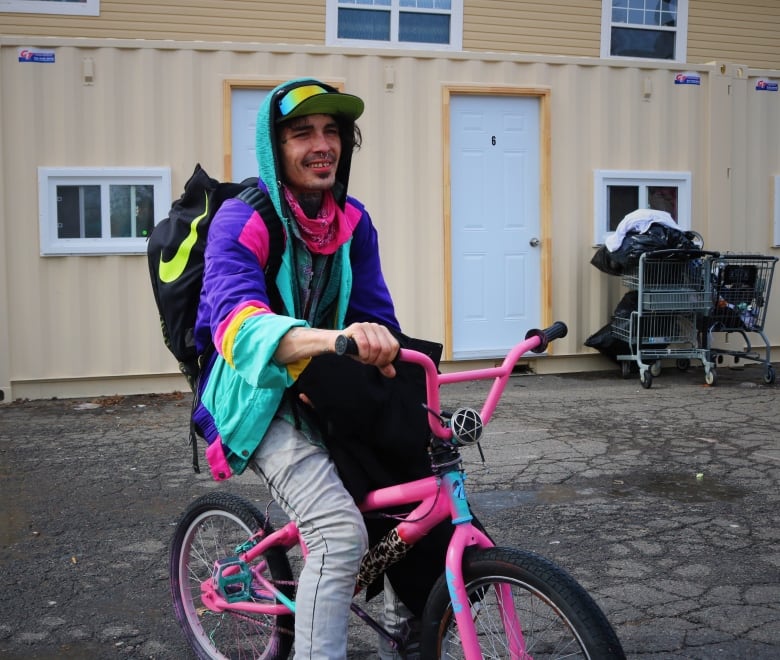 A man in bright clothing rides a pink BMX bike. 