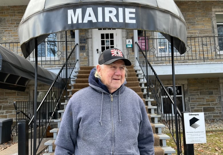 a man in a hoodie and a warrior hat stands outside an old stone building