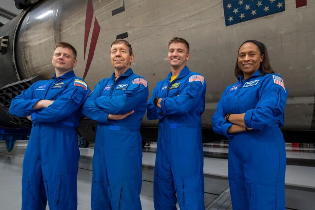 Russian cosmonaut Alexander Grebenkin, pilot Michael Barratt, commander Matthew Dominick, and astronaut Jeanette Epps pose with a Falcon 9 rocket inside SpaceX's hangar in Florida.