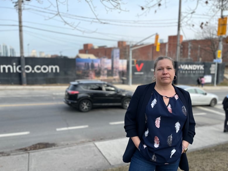 A woman stands across the street from a vacant lot next to a train station