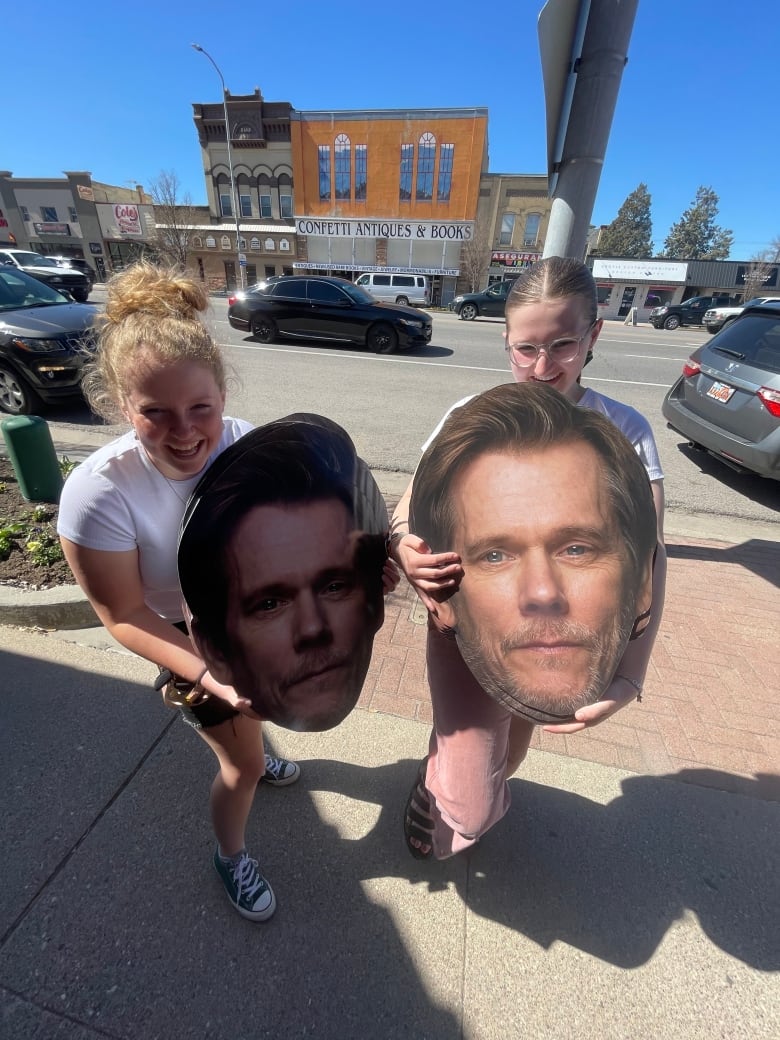 Two teenage girls hold large cut out faces of Kevin Bacon.