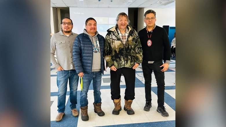 Four people stand in a row inside a room.