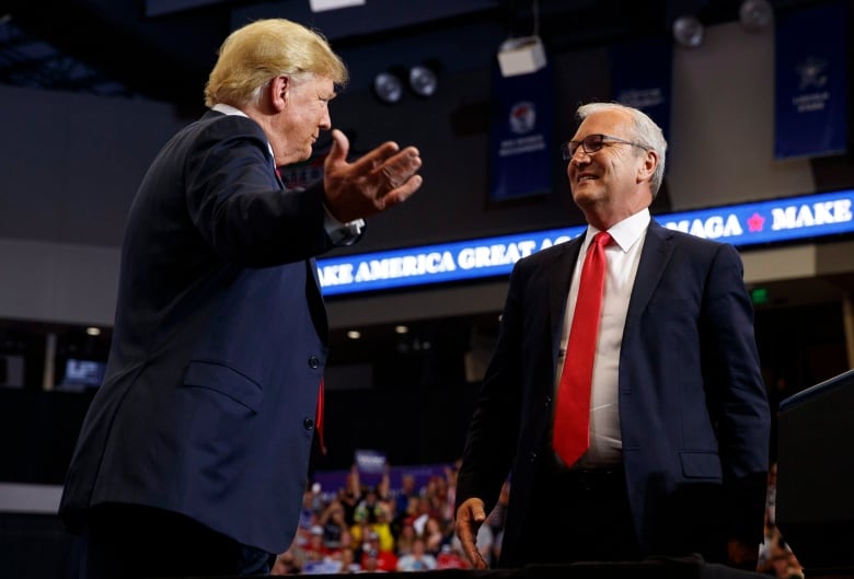 Trump opens arms on stage, with man in front of him