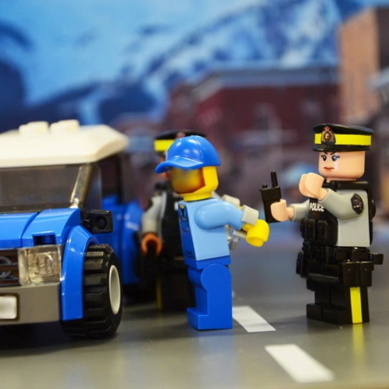 A toy lego police officer arrests a lego man. 