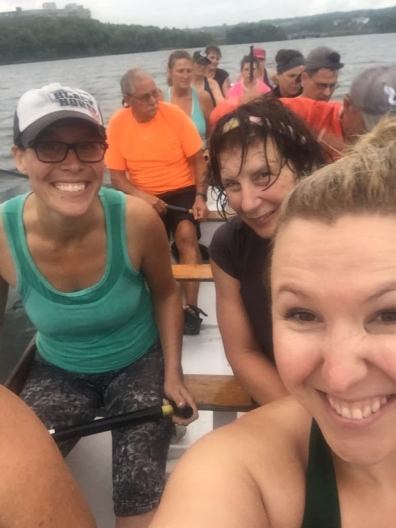 Several smiling people sit in a long boat on a lake. 