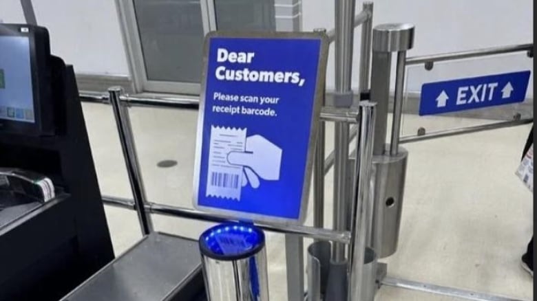 A device next to a metal gate has a sign that says, "Please scan your receipt barcode."