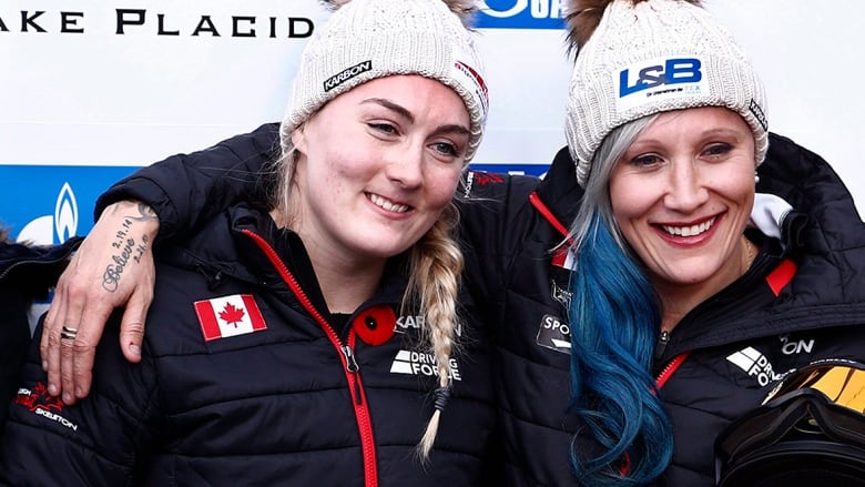 Two Canadian bobsledders, wearing beige toques and dark jackets, pose for photos after winning a women's two-person World Cup bobsled race in Lake Placid, N.Y., on Nov. 9, 2017.