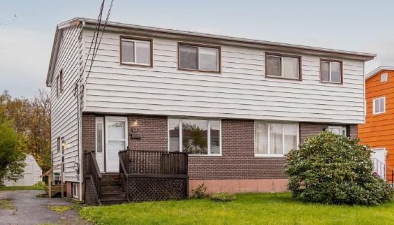 The street view of a two-storey duplex with brick on the ground floor and beige siding on the second, with multiple windows and a grassy lawn