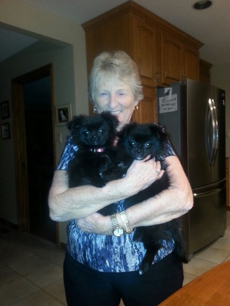 A smiling woman holds two small black dogs in her arms. 