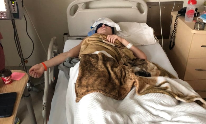 A young woman lies in a hospital bed with her eyes covered