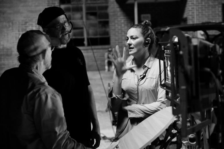 A woman speaks to two men on a film set.