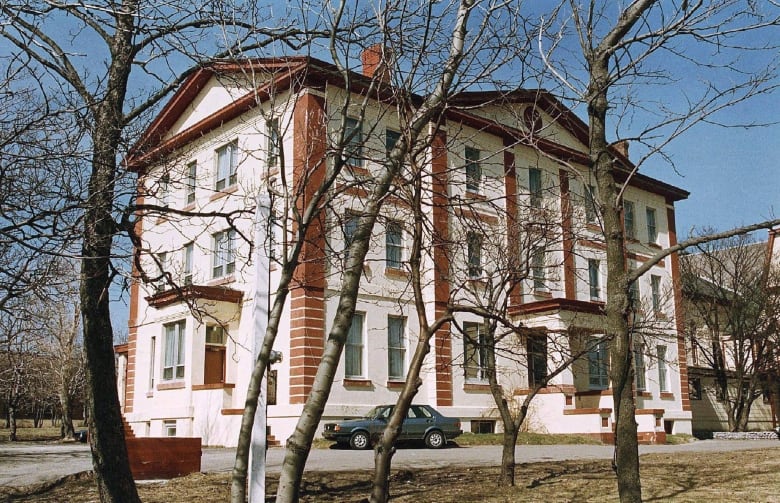 A white and red brick building is pictured through trees.