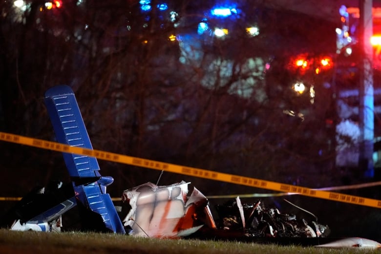 A night view of the wreck of a small plane that crashed on a grassy area, with yellow police tape stretch across the site. 