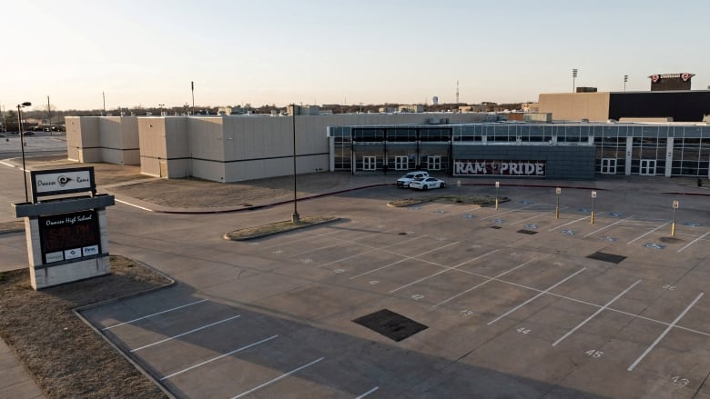 A wide view of a high school and a large parking lot. 