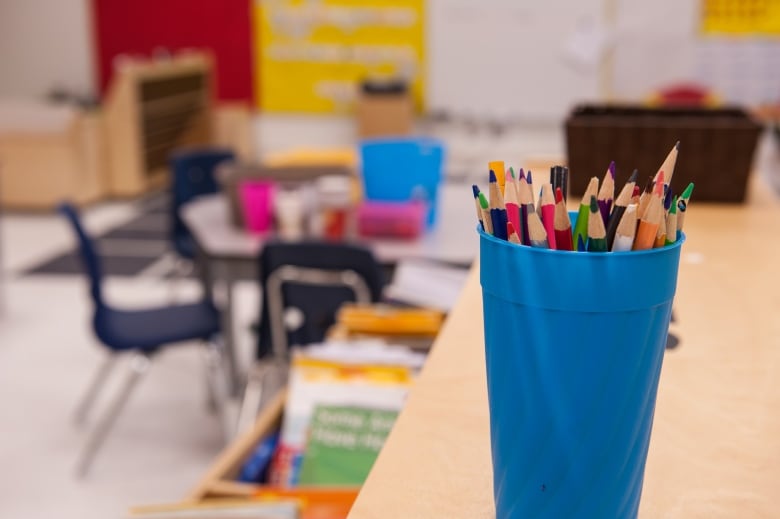 Coloured pencils in a blue cup stand on a desk in empty classroom