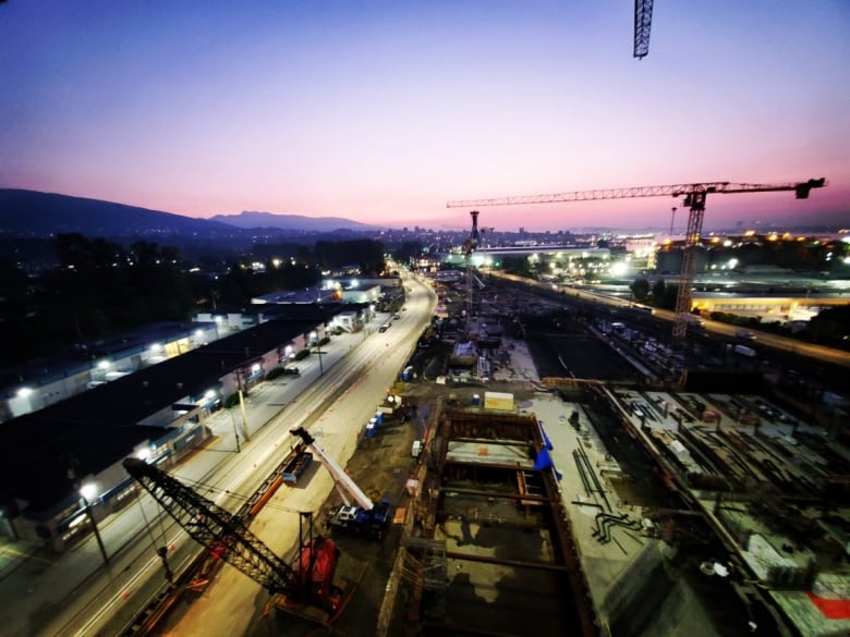 A construction site with a crane in the background and heavy equipment with a sunset in the background shows the very early stages of the building of the plant.