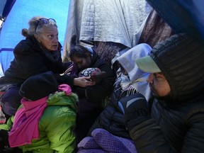 FILE - Medical volunteer Karen Parker, left, touches a 2-year-old child with a fever as she talks to a family of asylum-seeking migrants as they wait to be processed in a makeshift, mountainous campsite after crossing the border with Mexico, Feb. 2, 2024, near Jacumba Hot Springs, Calif. A federal judge on Friday, March 29, sharply questioned the Biden administration's position that it bears no responsibility for housing and feeding migrant children while they wait in makeshift camps along the U.S-Mexico border.