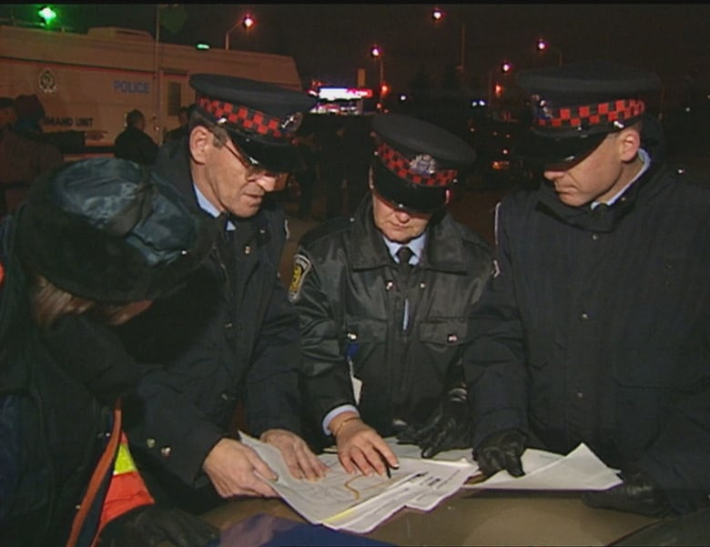 Police outdoors at night, huddled together looking at papers.