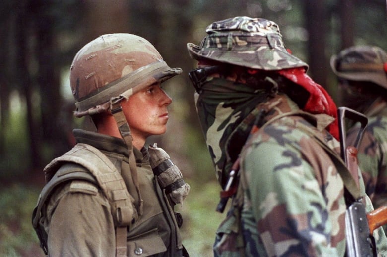 A soldier in a helmet and a Mohawk Indigenous Canada stare each other down. 