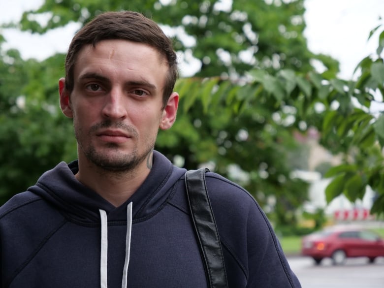 A man with brown hair. He's wearing a blue sweater and black backpack.