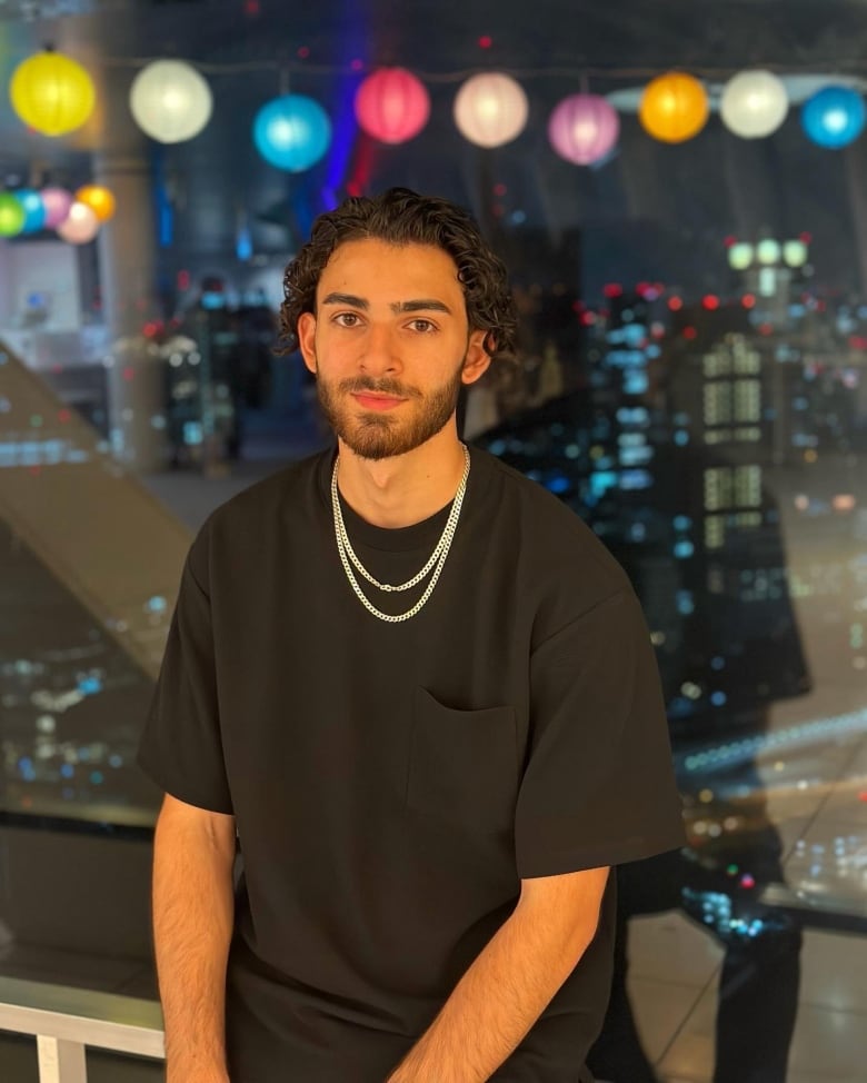 Man with black shirt and curly hair smiles.