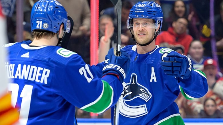 Two Canucks players look at each other on the ice, reacting to their team scoring goal during a March 23, 2024 NHL game against the Calgary Flames in Vancouver.