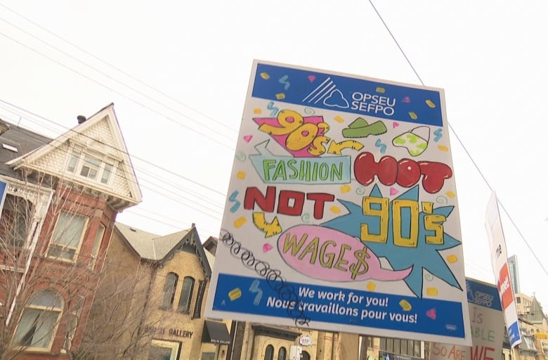 A colourful sign says, "90's fashion HOT not 90's WAGE$."