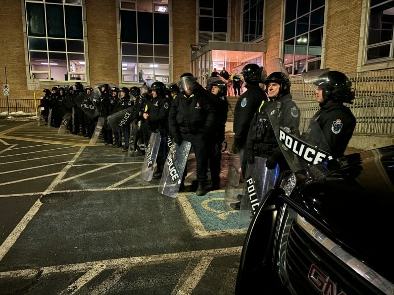 A line of police officers in riot gear standing in front of a building.