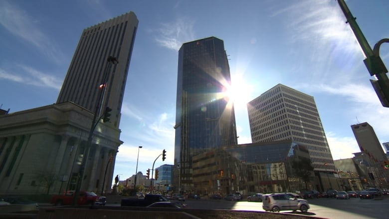 Sun shines past a tower in downtown Winnipeg as vehicles are seen passing through an intersection.