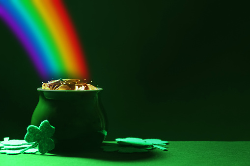 Pot with gold coins and clover leaves on green table, space for text. St. Patrick