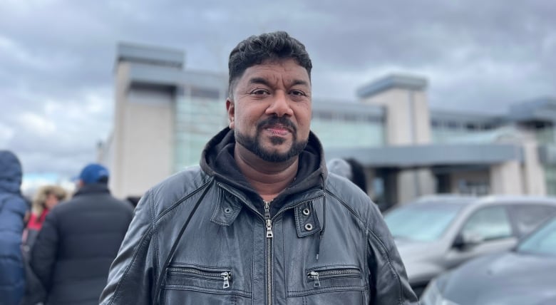 A man wearing a black leather jacket with a black beard looks into the camera.