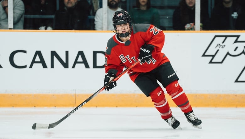 A female hockey player wearing a red Ottawa jersey skates on the ice.