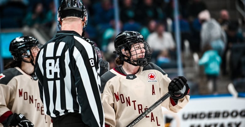 A hockey player with a Montreal jersey, with an A in the corner, holds her stick and looks to the side.