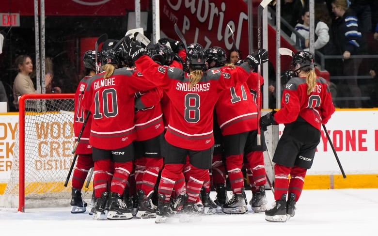 A group of hockey players in red jerseys celebrate on the ice.