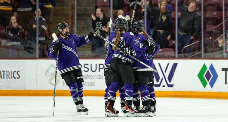 Several hockey players in purple jerseys celebrate on the ice.