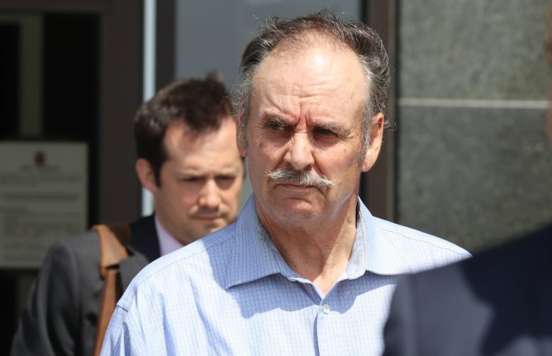 A man with a receding hairline and a moustache exits a building. 