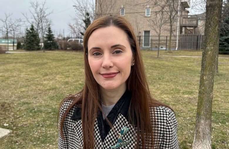 A woman in a chequered jacket, standing outside in a park, smiles for the camera.