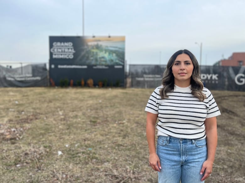 A woman stands on the grass in front of a sign for a failed housing development.