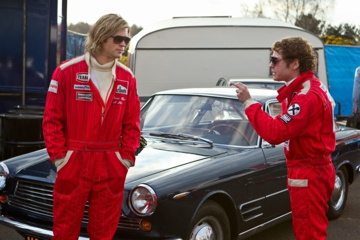 Two men talk next to a car in Rush.