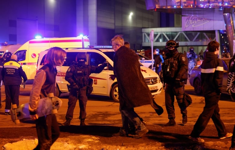 People muster outside at night among a number of armed police outside a building following an attack. 