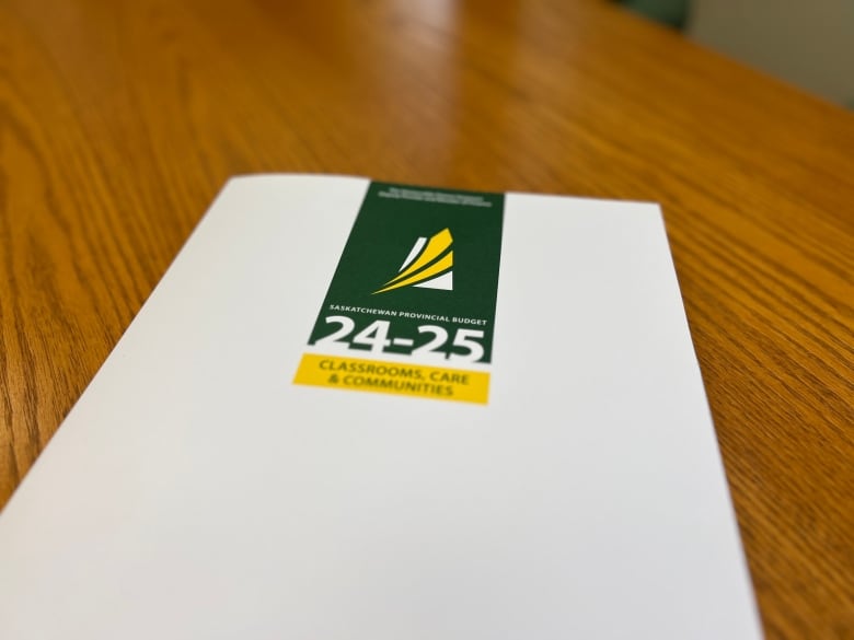 A white hardcover book sits on a wooden table. The booklet has a green and yellow logo and is titled 'Classrooms, Care and Communities.'