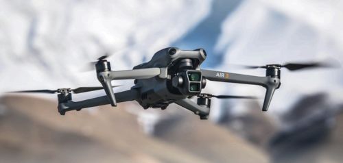 The DJI Air 3 in flight with a snowy mountain view blurred in the background.