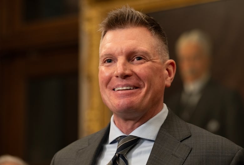 A man in a business suit smiles broadly. 