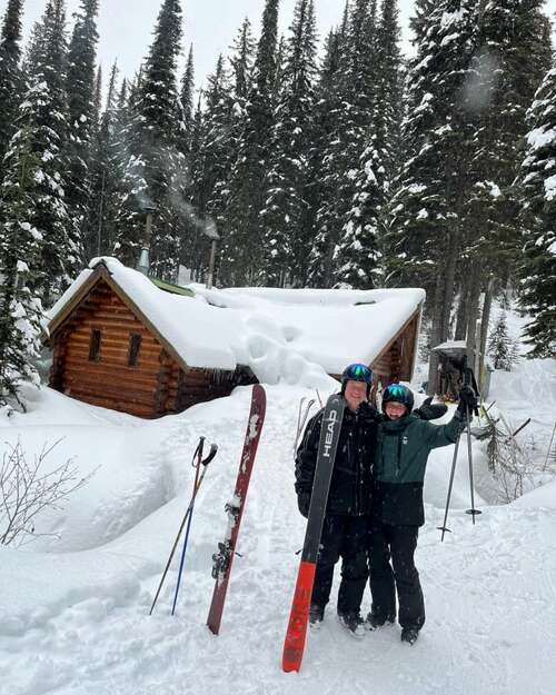 A man and a girl in front of a cabin in the snow.