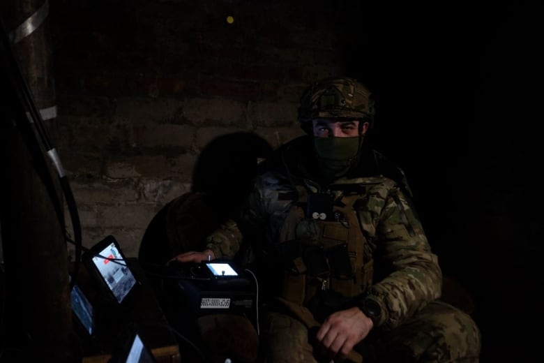 A man wearing combat gear in a dark room with screens around him.