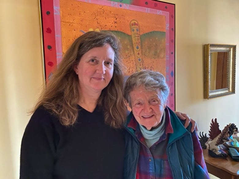 Two women stand together in front of a painting.