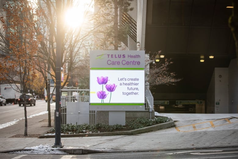 A sign for Telus Health Care Clinic is shown at the entrance to an industrial driveway.