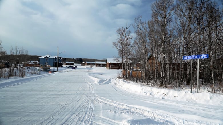 A photo of a snowy road on the Tsuut'ina reserve in Alberta. Trees and a few houses are visible in the background.