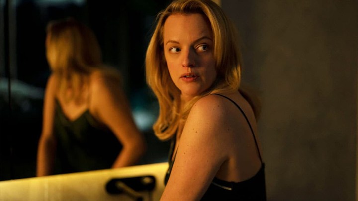 Elisabeth Moss standing by a mirror, looking behind her in a scene from The Veil.